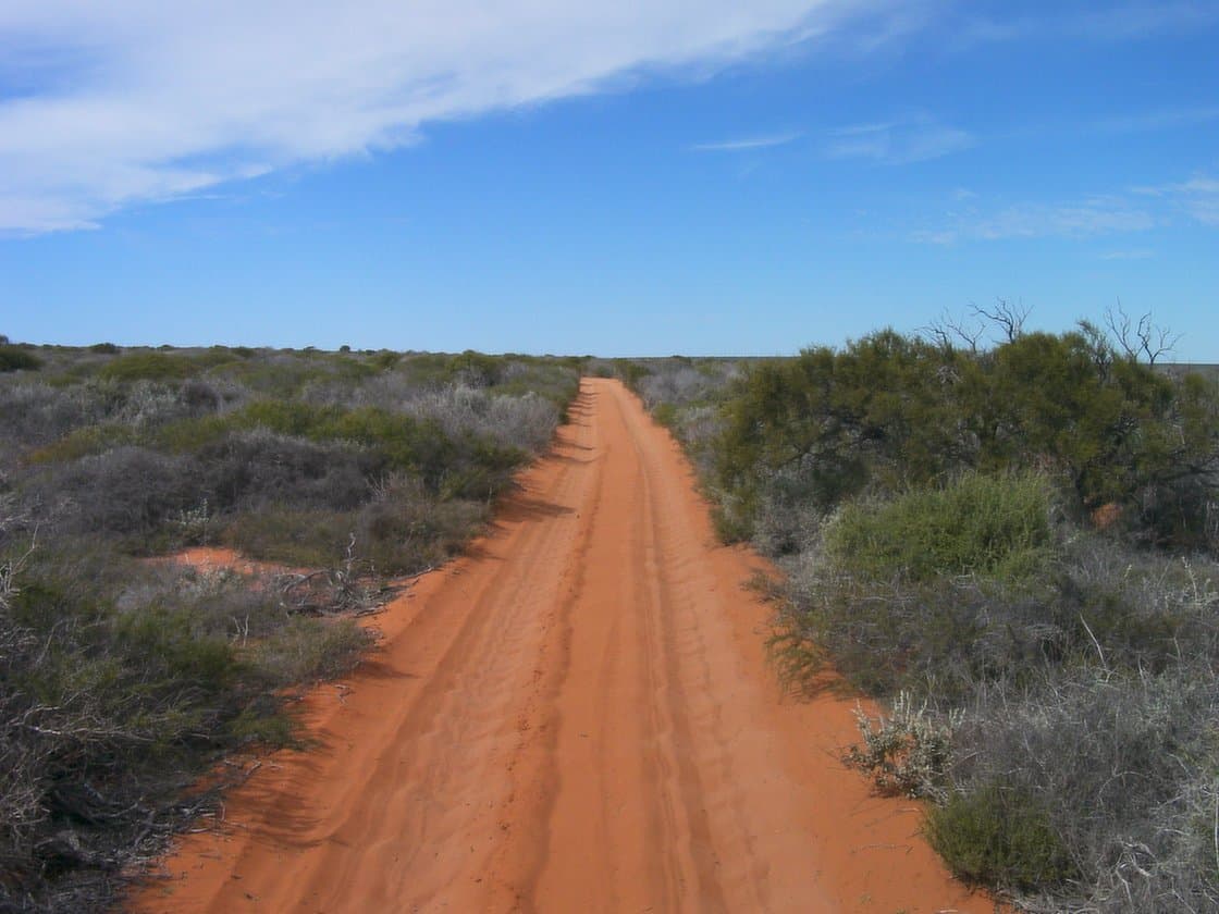Red-dirt touring track through low Australian scrub